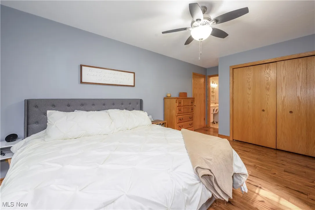 Bedroom with wood finished floors, connected bathroom, a closet, and ceiling fan