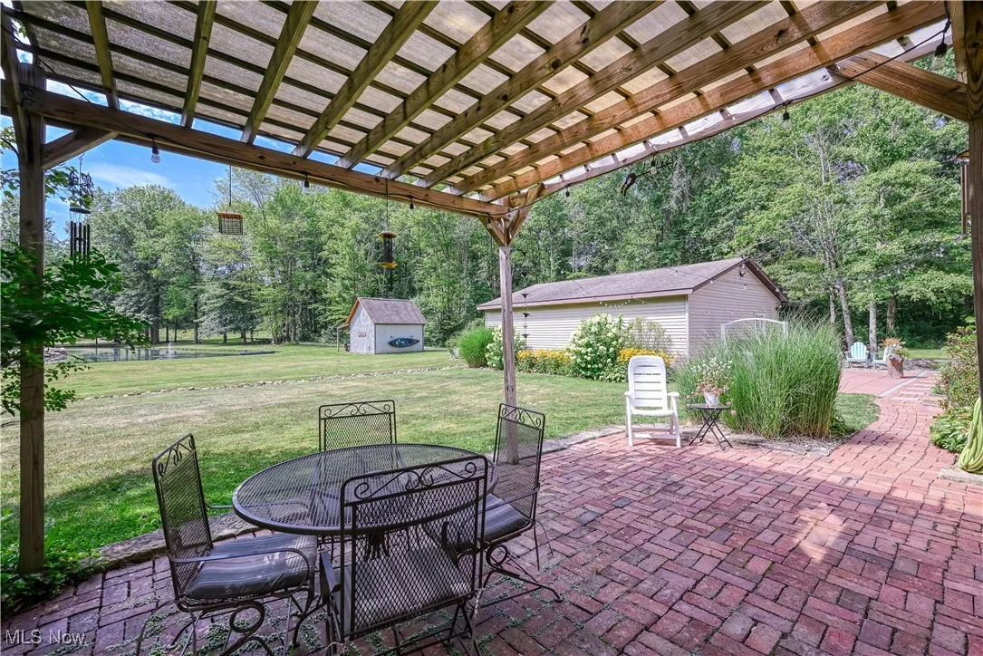View of patio featuring outdoor dining space, a storage shed, view of wooded area, and a pergola
