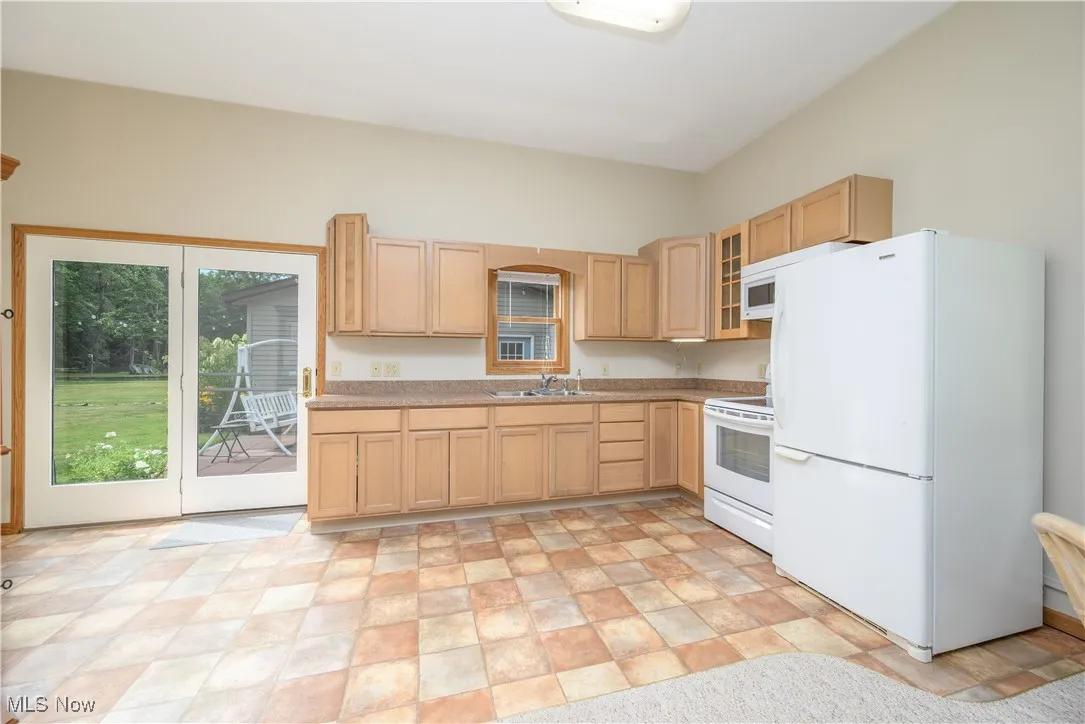 Kitchen featuring white appliances, light brown cabinets, light countertops, glass insert cabinets, and stone finish flooring