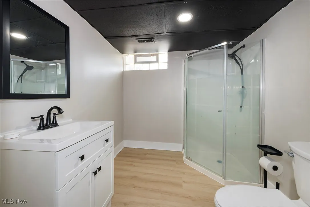 Bathroom with a shower stall, vanity, wood finished floors, and recessed lighting