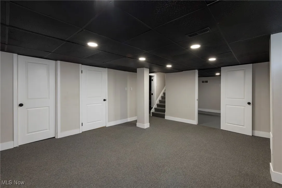 Finished basement featuring dark colored carpet, a drop ceiling, stairs, and recessed lighting