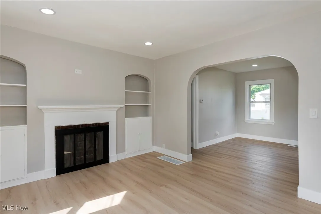 Unfurnished living room featuring built in features, a fireplace, recessed lighting, wood finished floors, and arched walkways