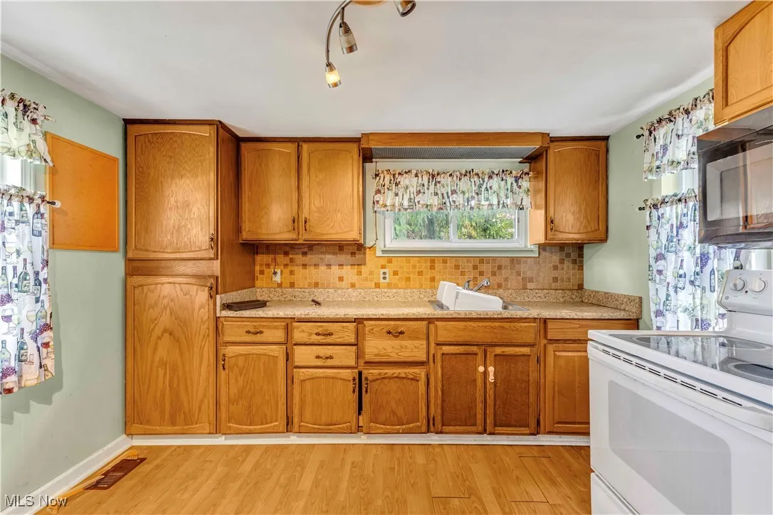 Kitchen with white electric stove, tasteful backsplash, light wood-type flooring, brown cabinetry, and light countertops