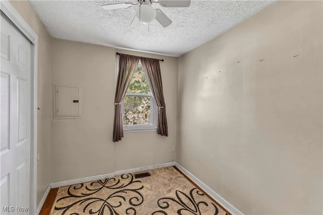 Empty room with electric panel, a ceiling fan, and a textured ceiling