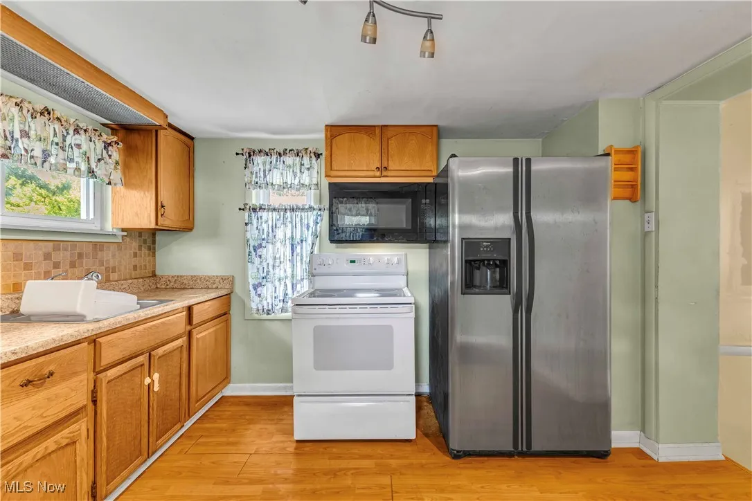 Kitchen featuring stainless steel fridge with ice dispenser, white range with electric stovetop, black microwave, light wood finished floors, and light countertops