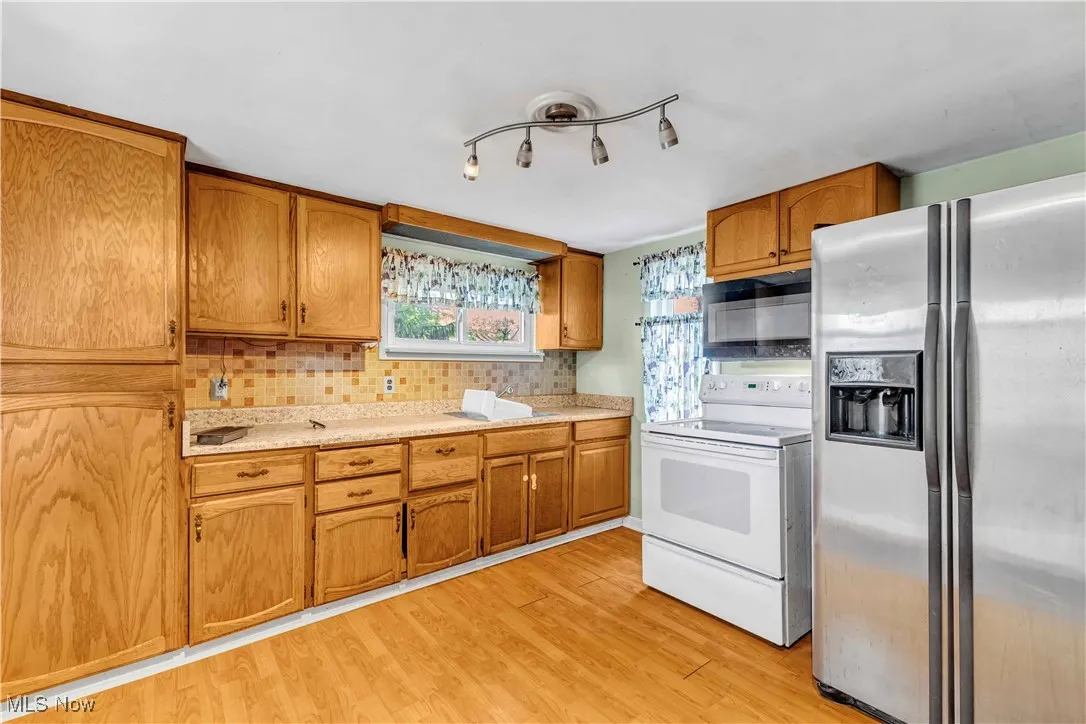 Kitchen with appliances with stainless steel finishes, brown cabinets, light countertops, and light wood-style floors