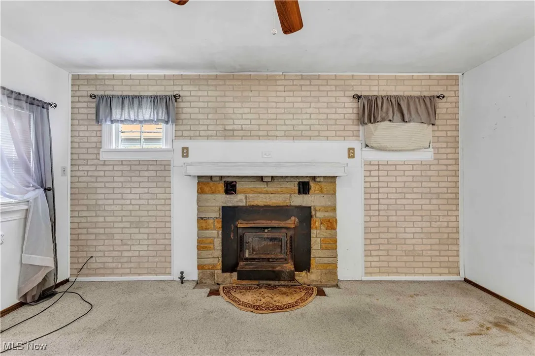 Carpeted living room featuring brick wall, a wood stove, and ceiling fan