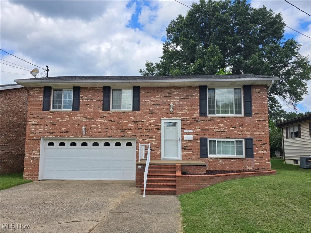 Bi-level home with brick siding, driveway, a garage, and a front yard