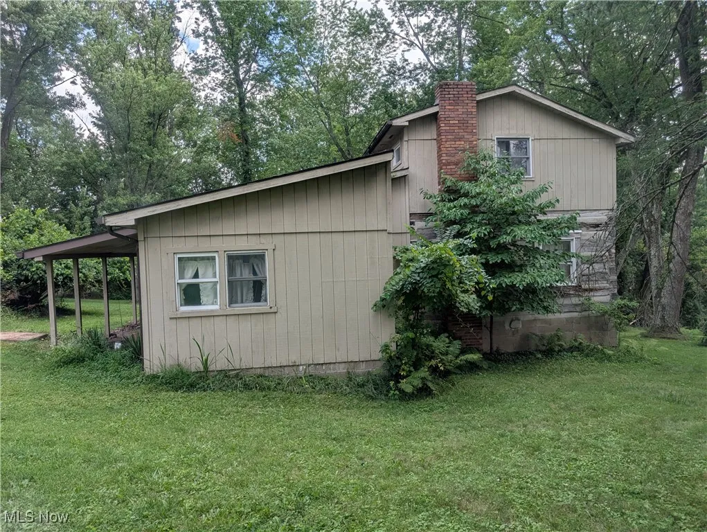 View of home's exterior with view of wooded area, a lawn, and a chimney