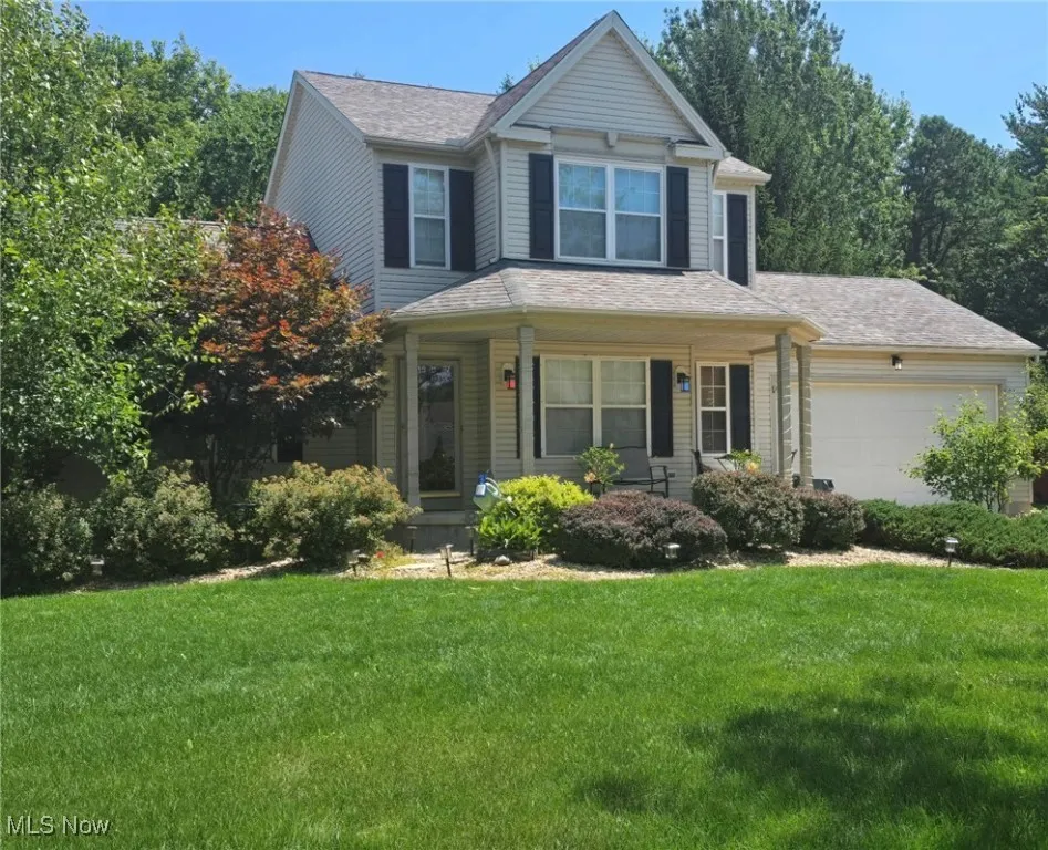 View of front of property featuring a front yard, a garage, and a shingled roof