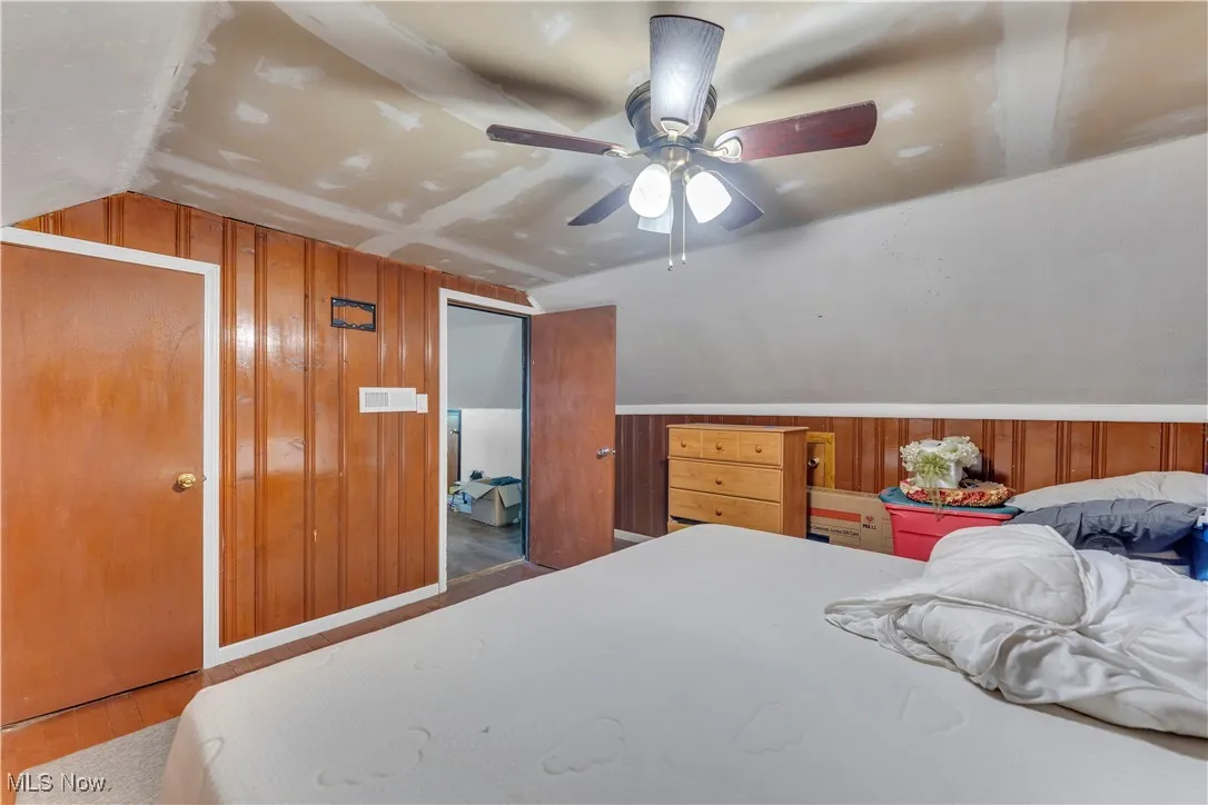 Bedroom featuring wood walls, lofted ceiling, wood finished floors, and a ceiling fan