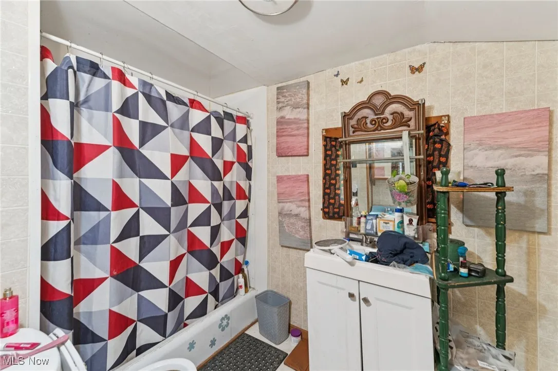 Bathroom featuring tile walls, vanity, shower / bath combo, and lofted ceiling