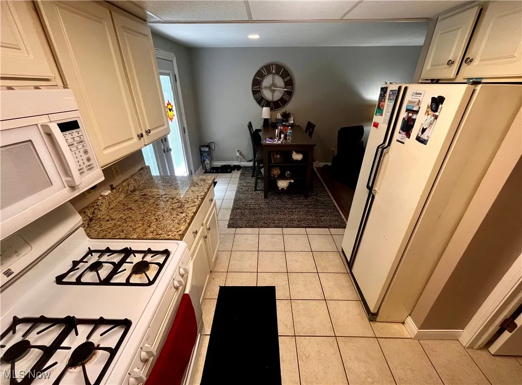 Kitchen with white appliances, light tile patterned floors, white cabinetry, and a drop ceiling