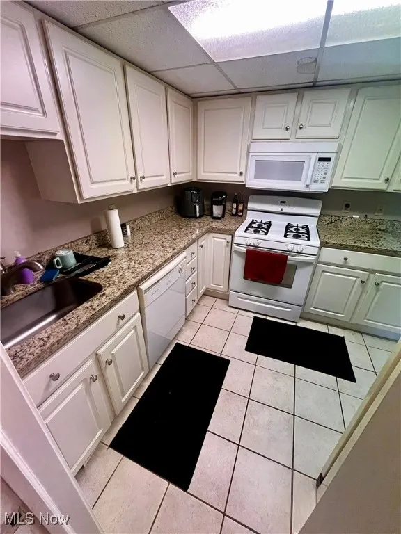 Kitchen with a paneled ceiling, white appliances, white cabinetry, and light tile patterned floors