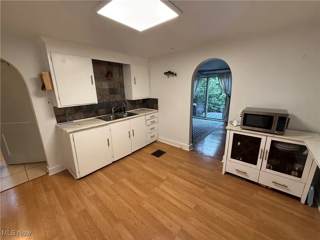 Kitchen featuring arched walkways, white cabinetry, decorative backsplash, stainless steel microwave, and light countertops