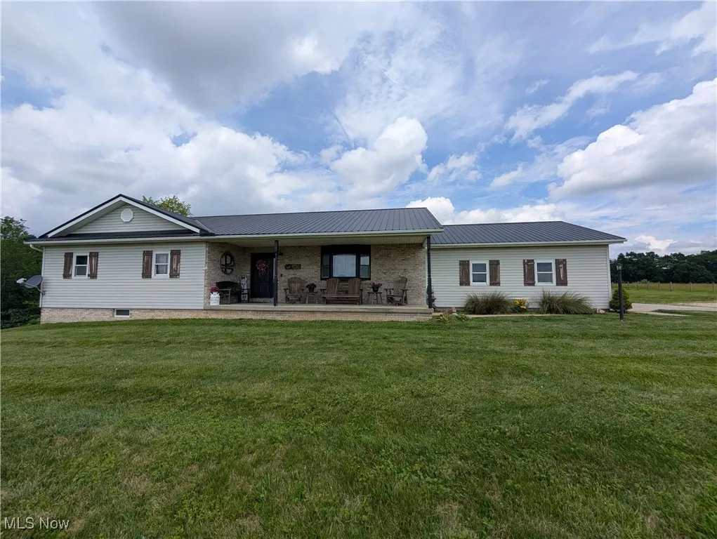 Ranch-style house featuring a front lawn, a porch, a metal roof, and brick siding