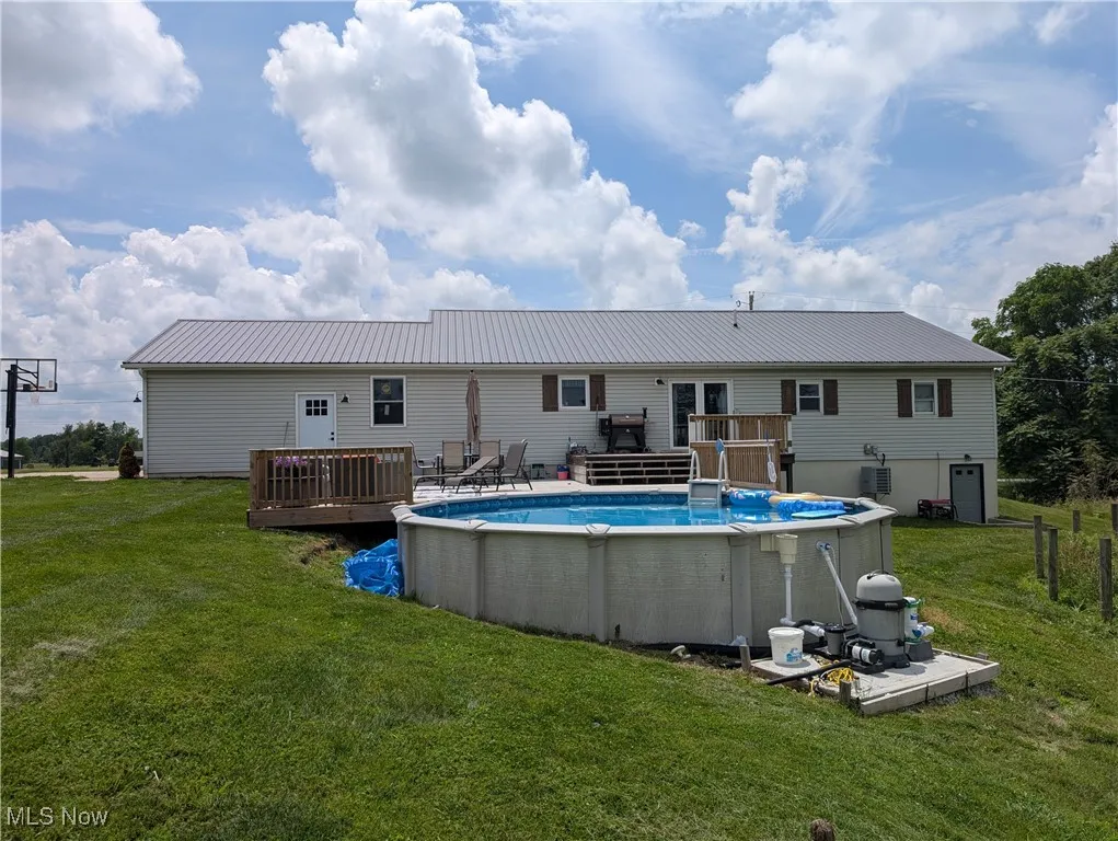 Back of property with an outdoor pool, a deck, a lawn, and a metal roof