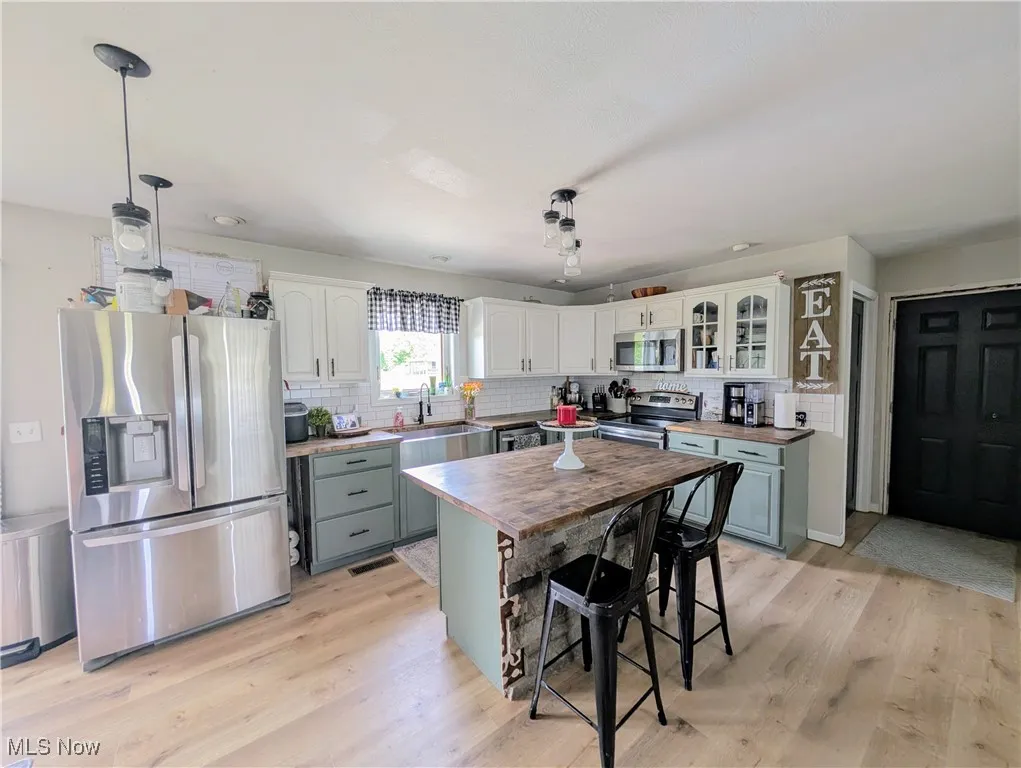 Kitchen with stainless steel appliances, butcher block countertops, tasteful backsplash, white cabinets, and light wood-type flooring