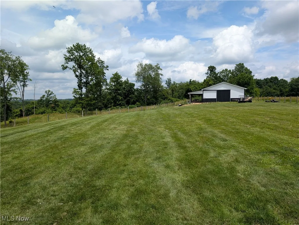 View of grassy yard featuring a pole building, a wooded view, a view of countryside, and an outbuilding