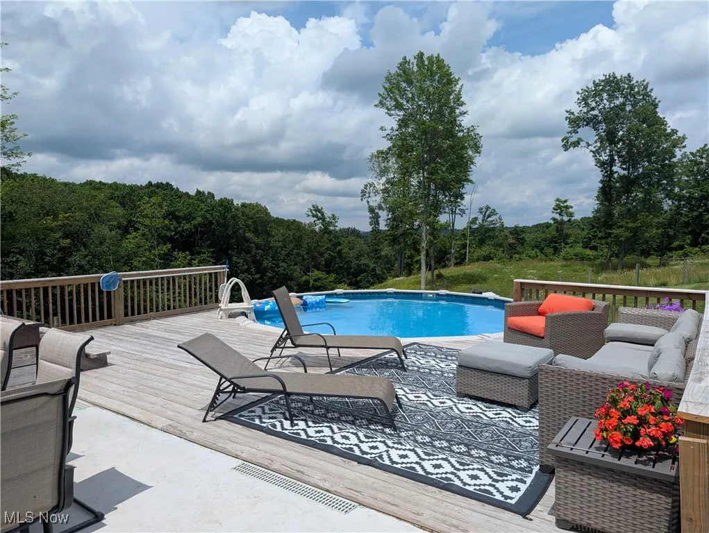 Outdoor pool with a wooden deck, outdoor lounge area, and a view of trees