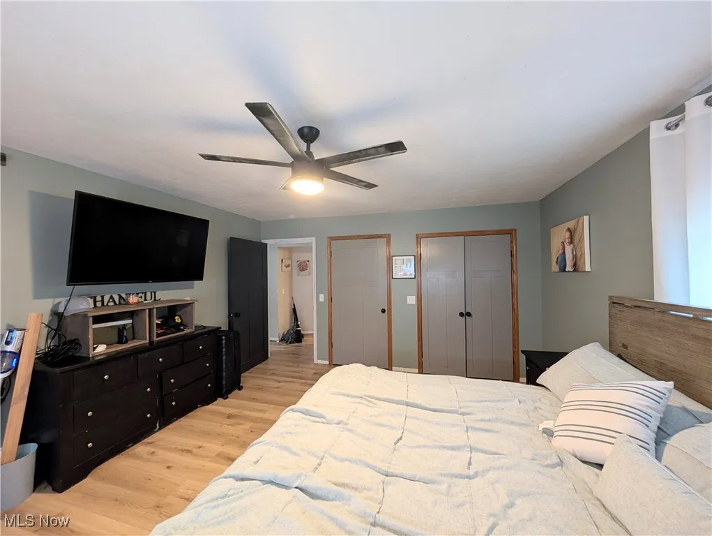 Bedroom with light wood-type flooring, two closets, and ceiling fan