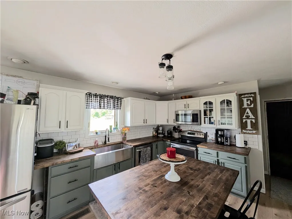 Kitchen with butcher block countertops, appliances with stainless steel finishes, backsplash, and white cabinetry