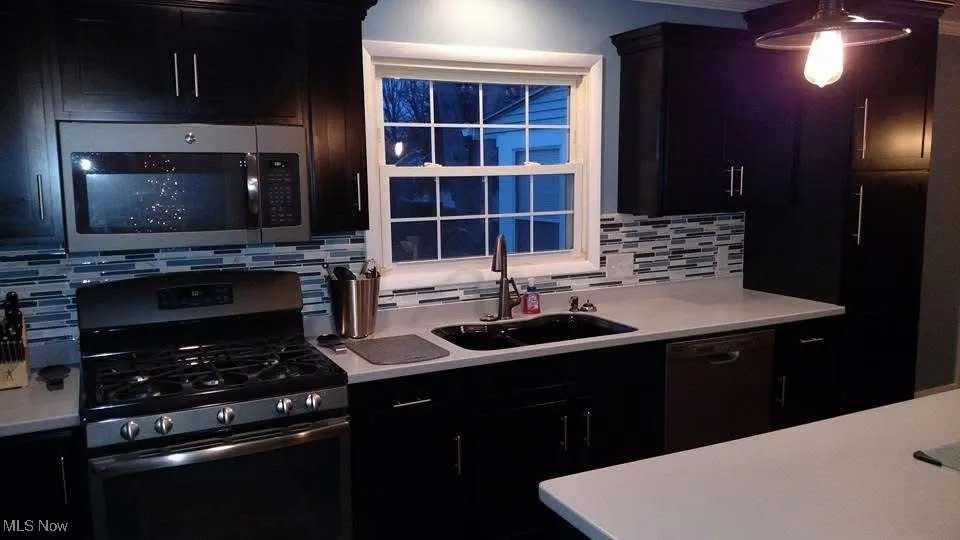 Kitchen with appliances with stainless steel finishes, light countertops, decorative backsplash, and dark cabinetry