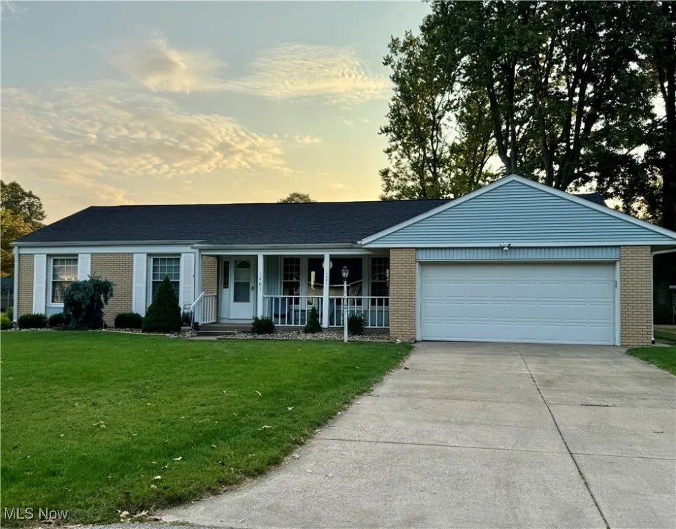 Ranch-style home with a front yard, brick siding, concrete driveway, an attached garage, and covered porch