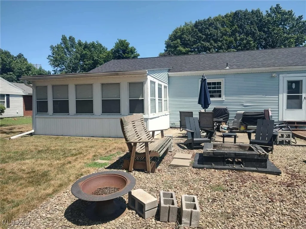 Rear view of house featuring a fire pit, a patio, roof with shingles, and a yard