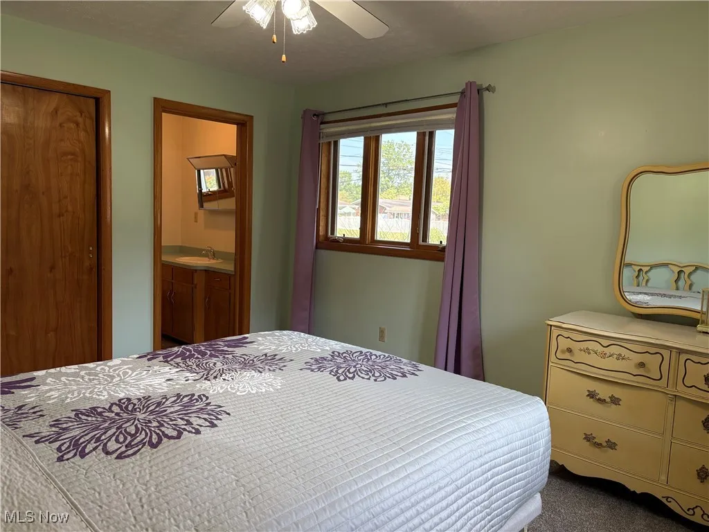 Bedroom with dark carpet, connected bathroom, and a ceiling fan