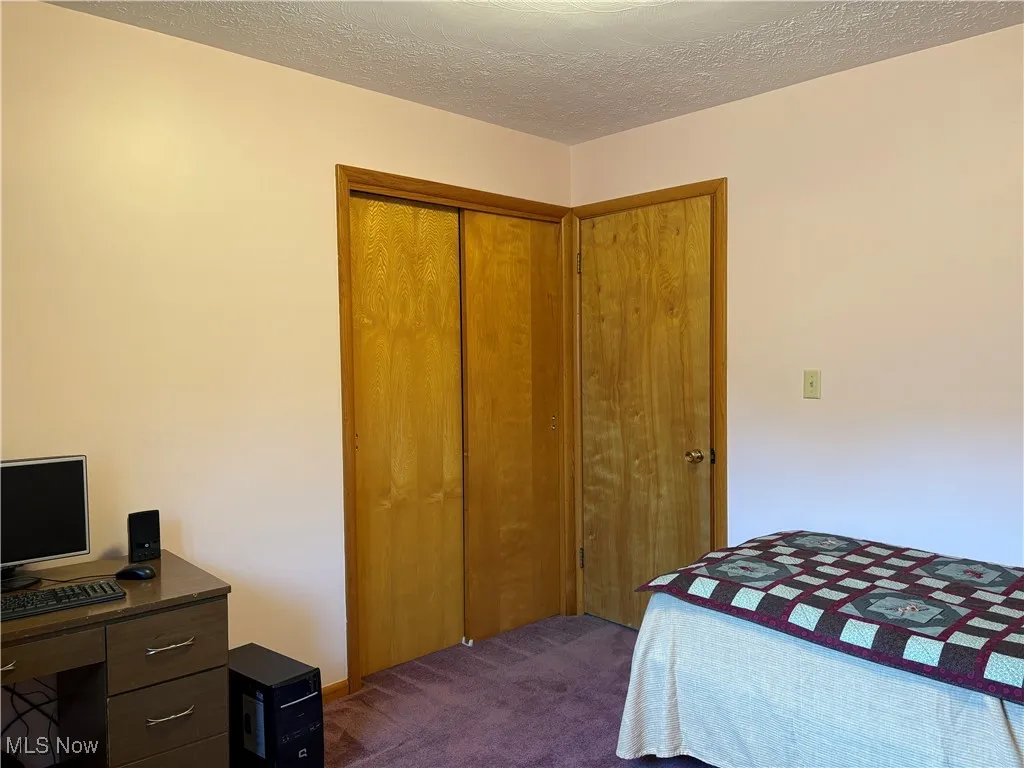 Bedroom featuring dark colored carpet, a textured ceiling, a closet, and a desk
