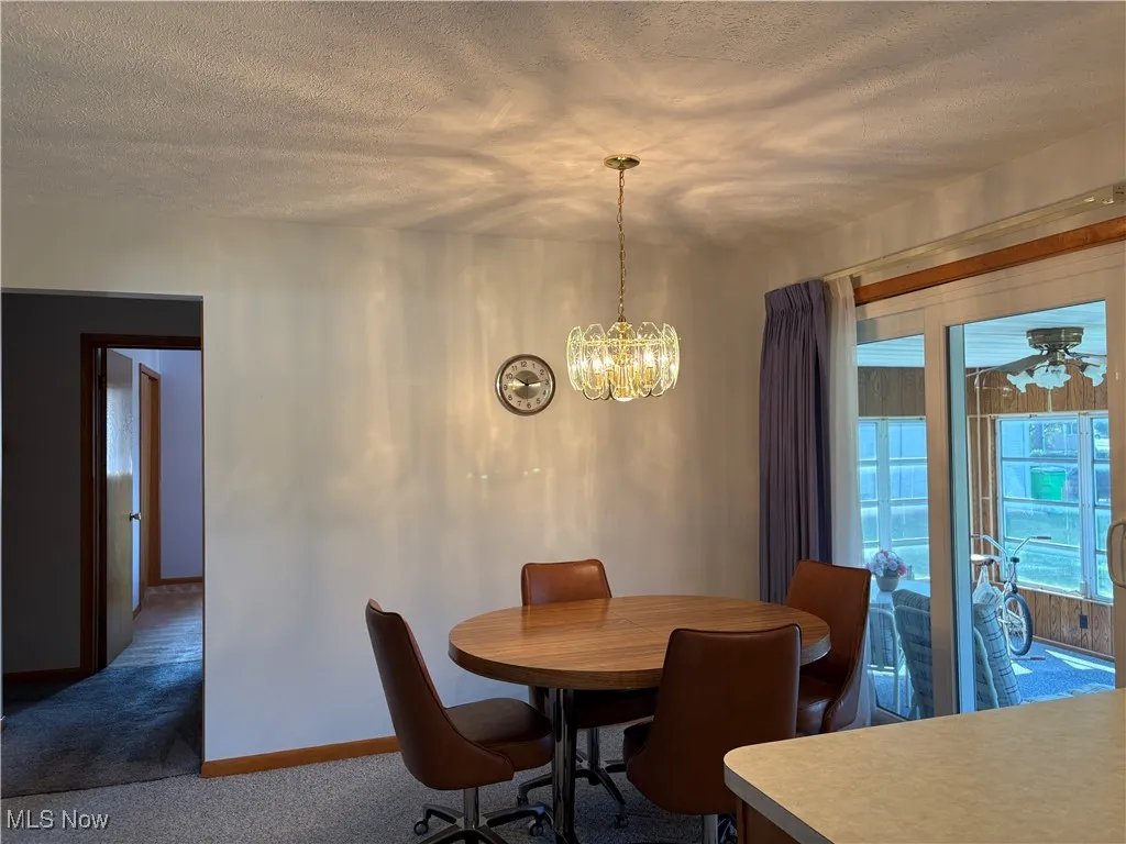 Carpeted dining space featuring a textured ceiling, a chandelier, and ceiling fan