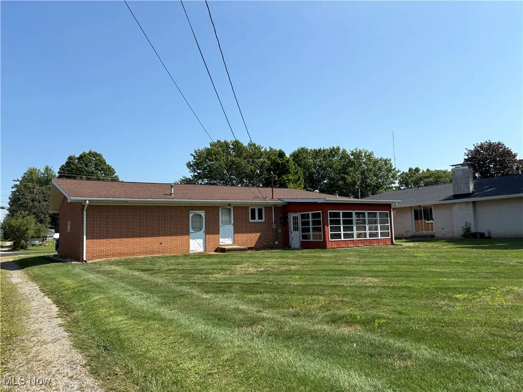 Back of house with a yard, a sunroom, and brick siding