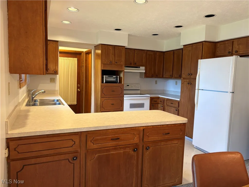 Kitchen featuring white appliances, a peninsula, light countertops, under cabinet range hood, and recessed lighting