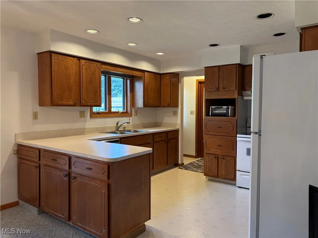 Kitchen featuring freestanding refrigerator, a peninsula, light flooring, recessed lighting, and light countertops
