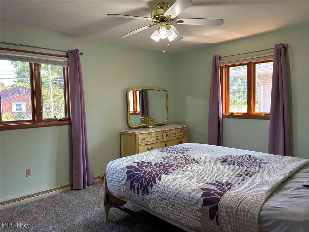 Carpeted bedroom with a baseboard heating unit and ceiling fan