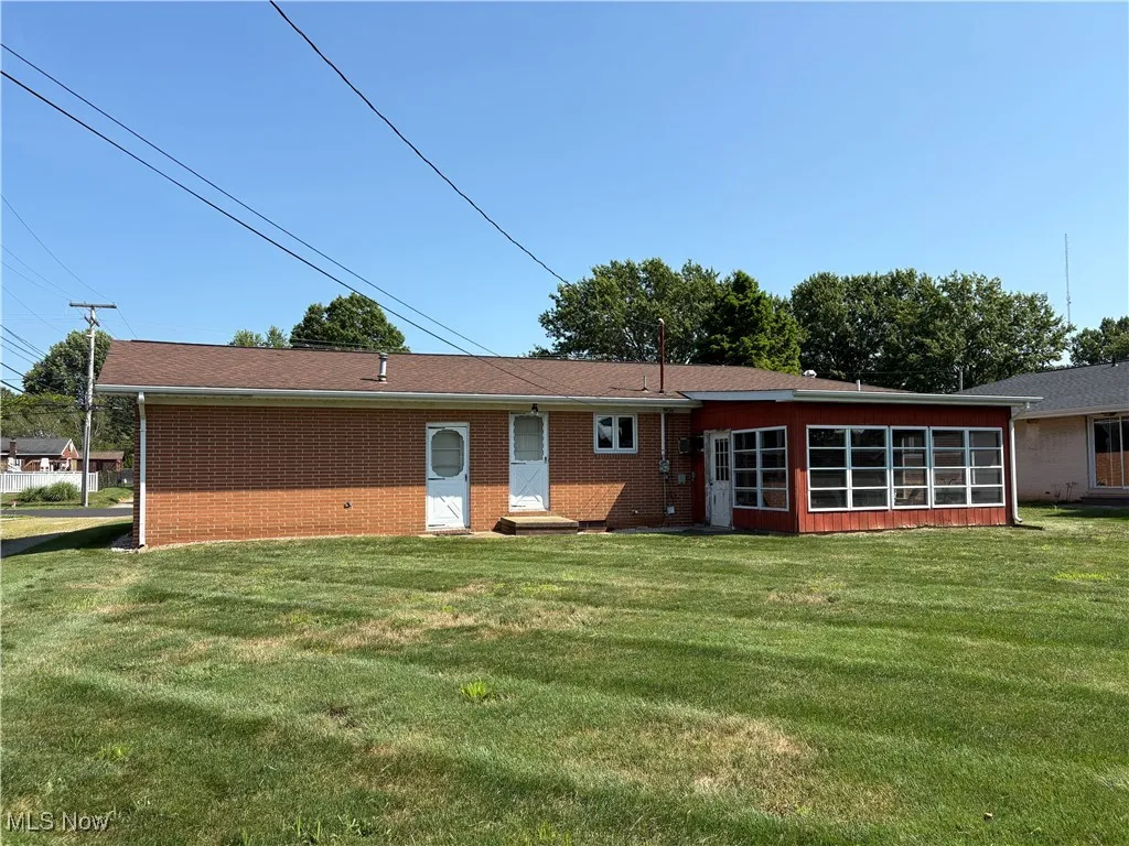 Back of property featuring a yard, a sunroom, brick siding, and entry steps