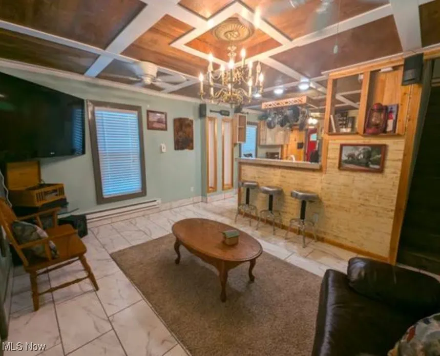 Living room featuring coffered ceiling, light marble finish floors, ceiling fan, a chandelier, and beam ceiling