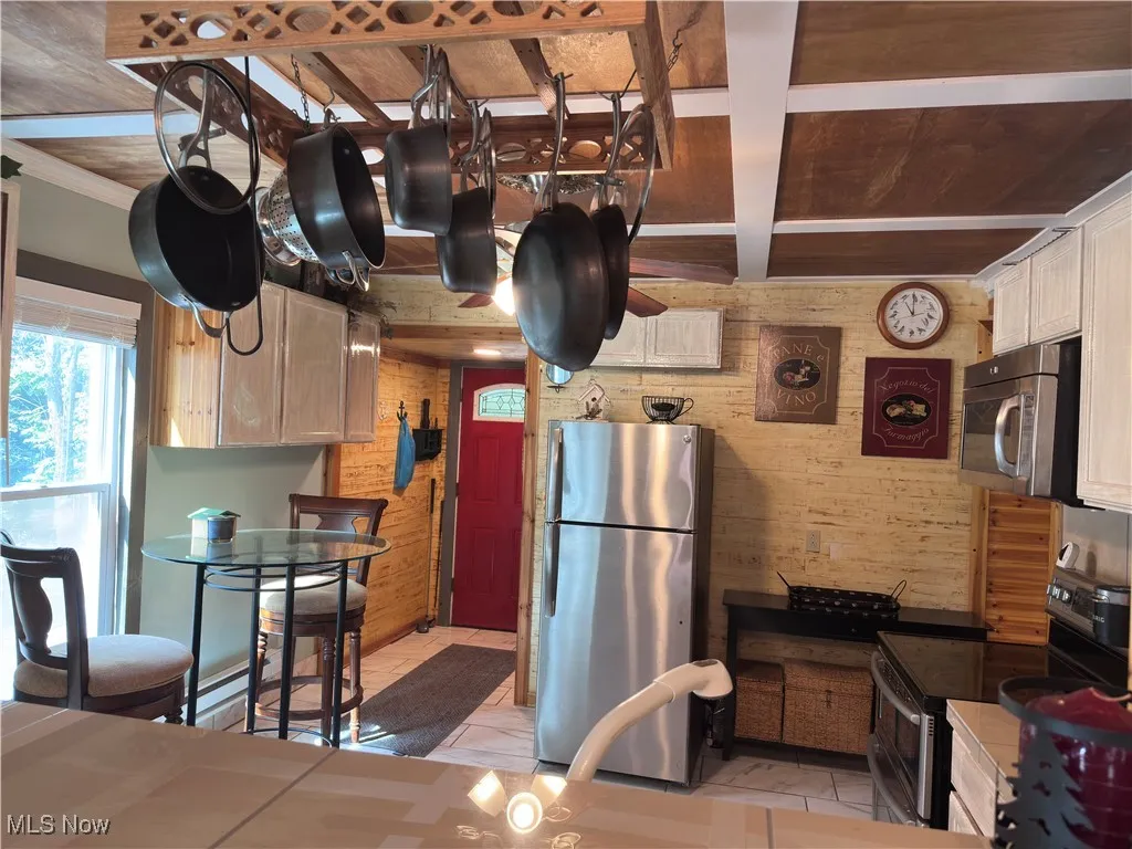 Kitchen with appliances with stainless steel finishes, wood walls, white cabinetry, and beamed ceiling