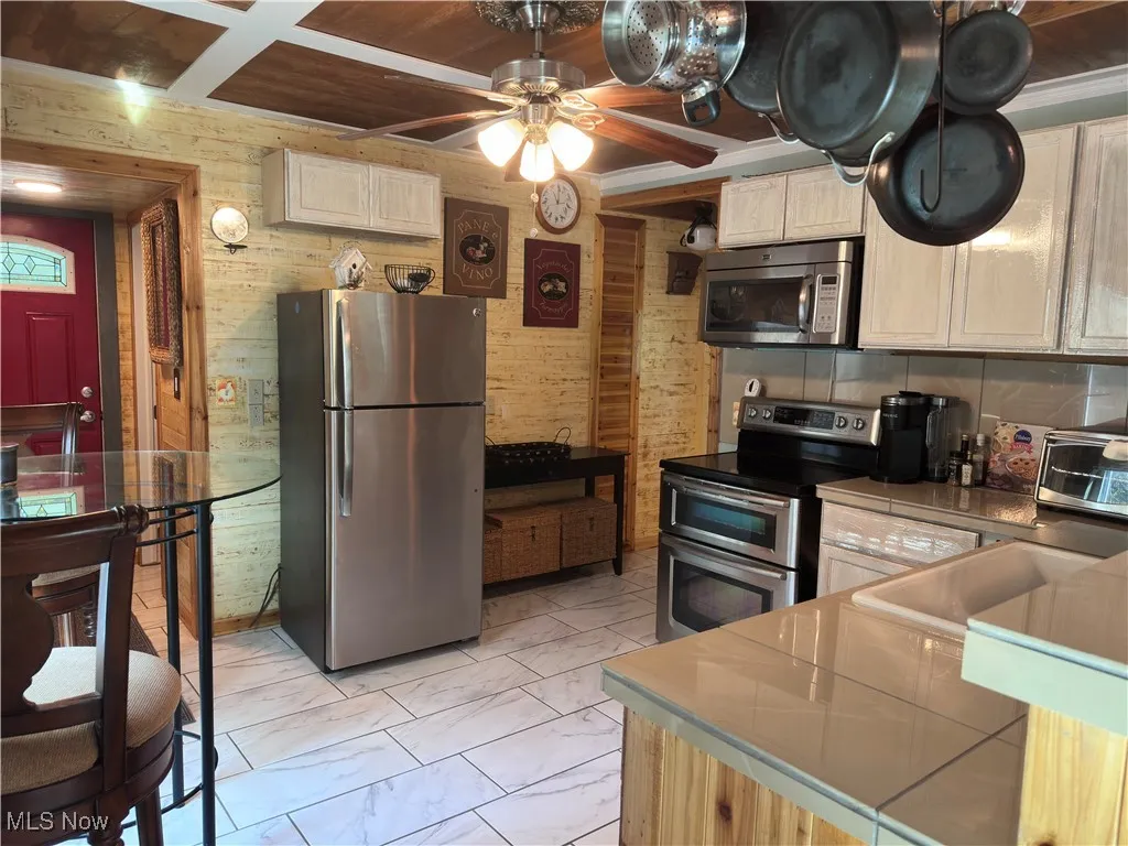 Kitchen with appliances with stainless steel finishes, a ceiling fan, light marble finish flooring, wooden walls, and wood ceiling