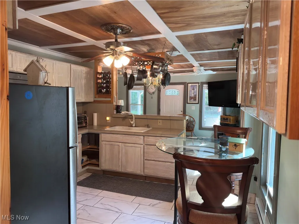 Kitchen featuring freestanding refrigerator, a wood ceiling with exposed beams, a peninsula, marble look tiles, and ceiling fan