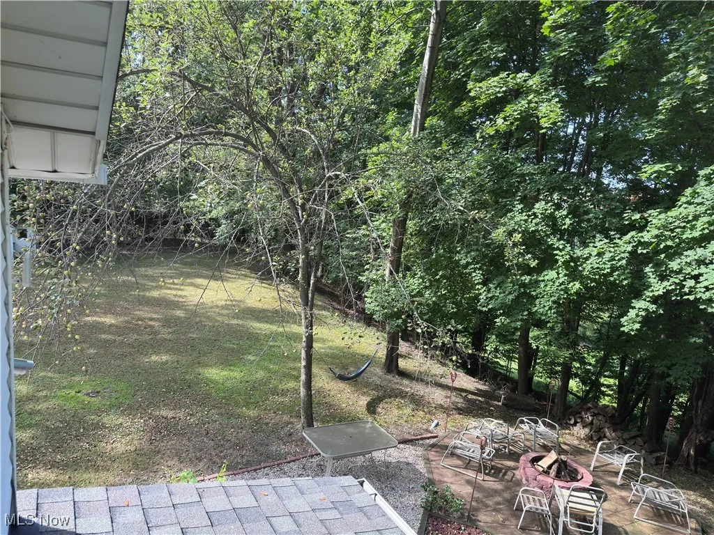 View of grassy yard featuring a patio, an outdoor fire pit, and view of scattered trees