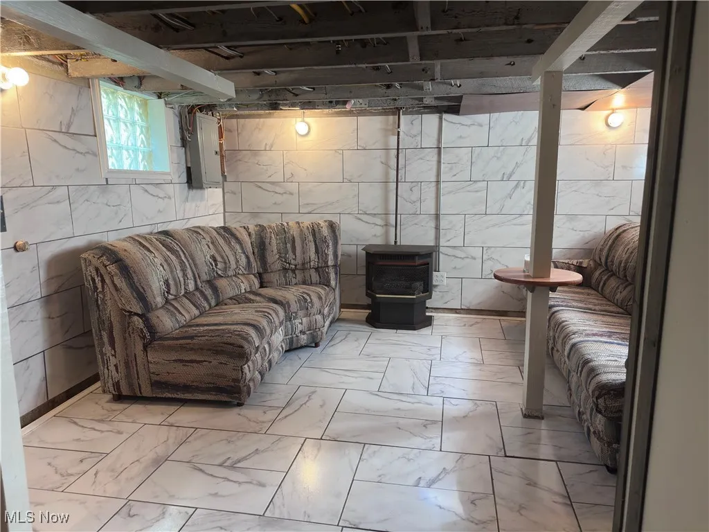 Basement featuring light marble finish flooring, a wood stove, and electric panel