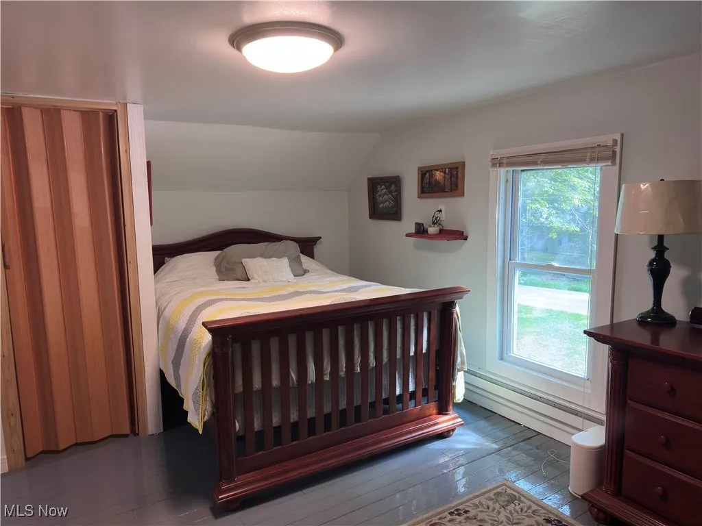 Bedroom with a baseboard heating unit, hardwood / wood-style flooring, and vaulted ceiling