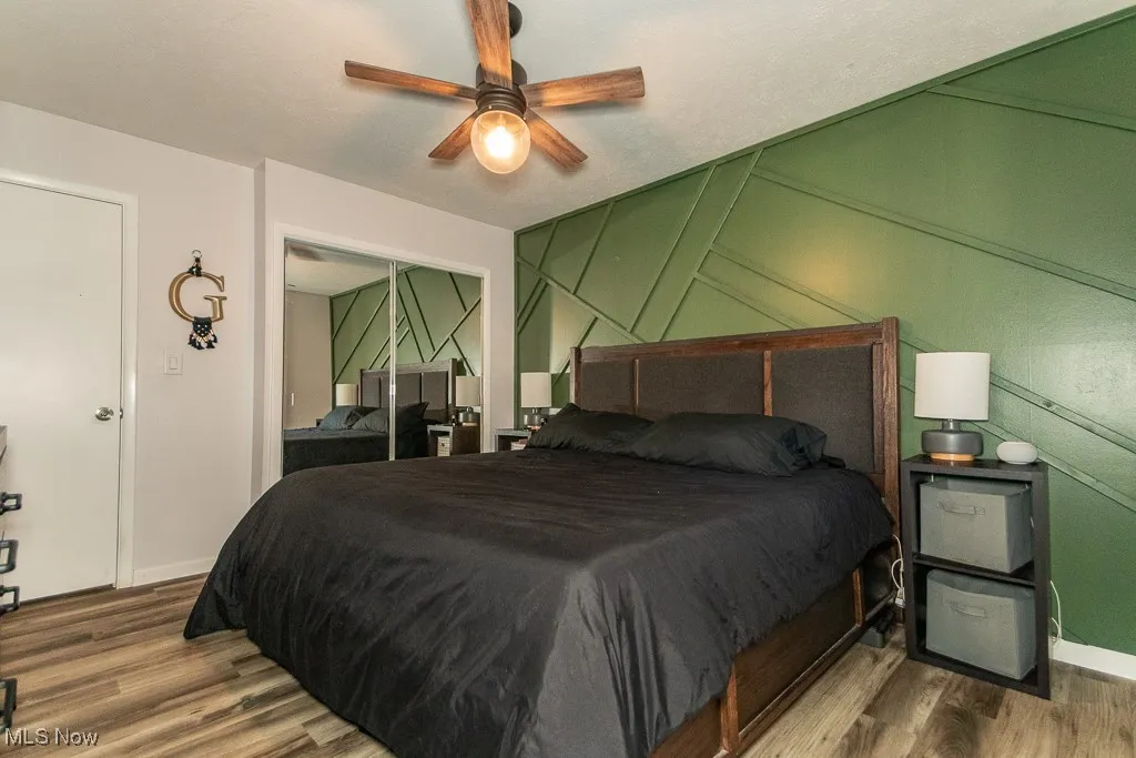 Bedroom with wood finished floors, a ceiling fan, a decorative wall, and a textured ceiling