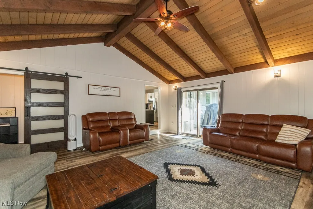 Living area with a barn door, a ceiling fan, wood finished floors, and wooden walls