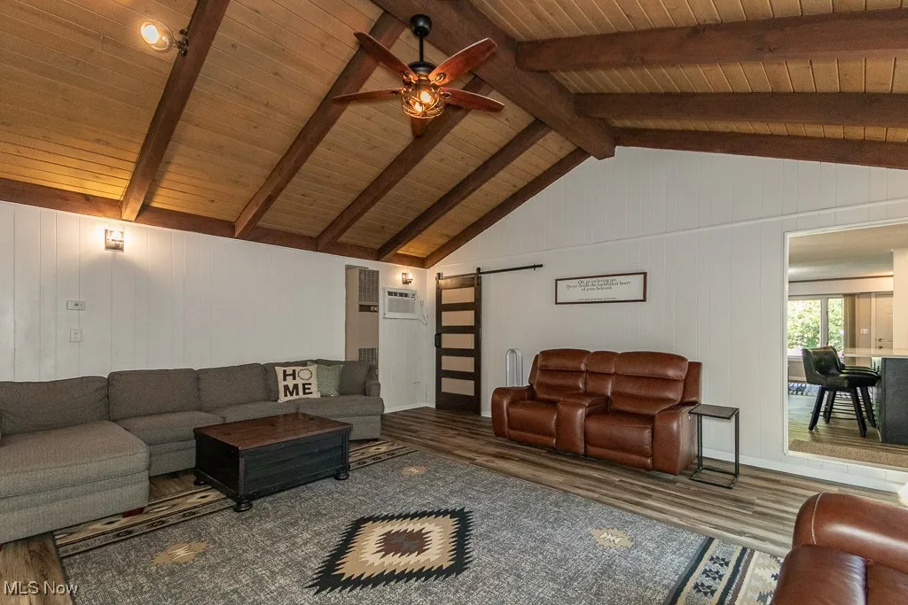Living room with a barn door, wood finished floors, wood walls, ceiling fan, and wooden ceiling