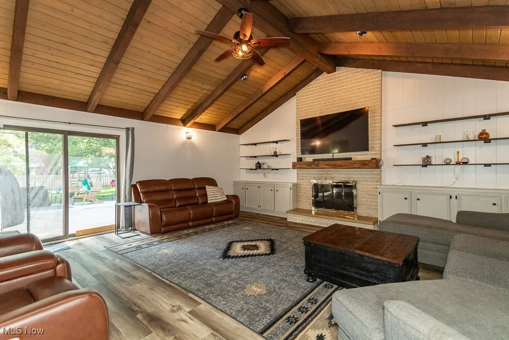Living room featuring wood finished floors, ceiling fan, a brick fireplace, and wooden ceiling
