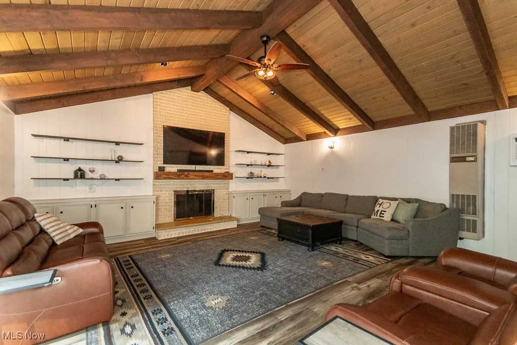 Living room with wood finished floors, a brick fireplace, a heating unit, wood ceiling, and a ceiling fan