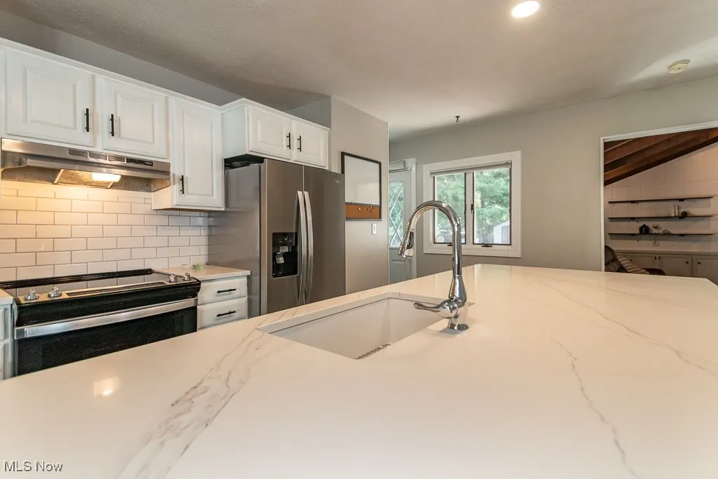 Kitchen with appliances with stainless steel finishes, decorative backsplash, under cabinet range hood, white cabinetry, and recessed lighting